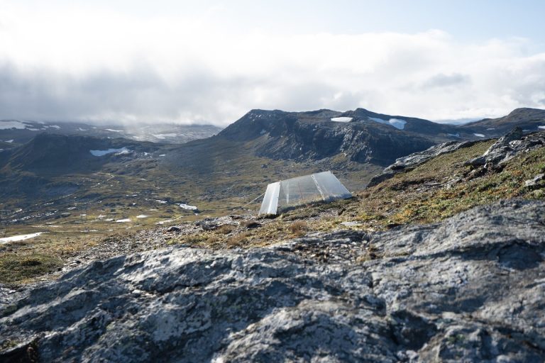 Ett ljust tunneltält på en klippig fjällplatå med snöfläckar på bergen bakom