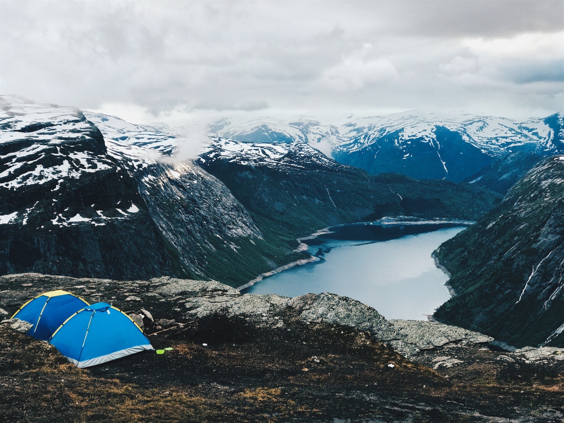 Två blå kupoltält på en klippa ovanför en fjord med snöklädda berg